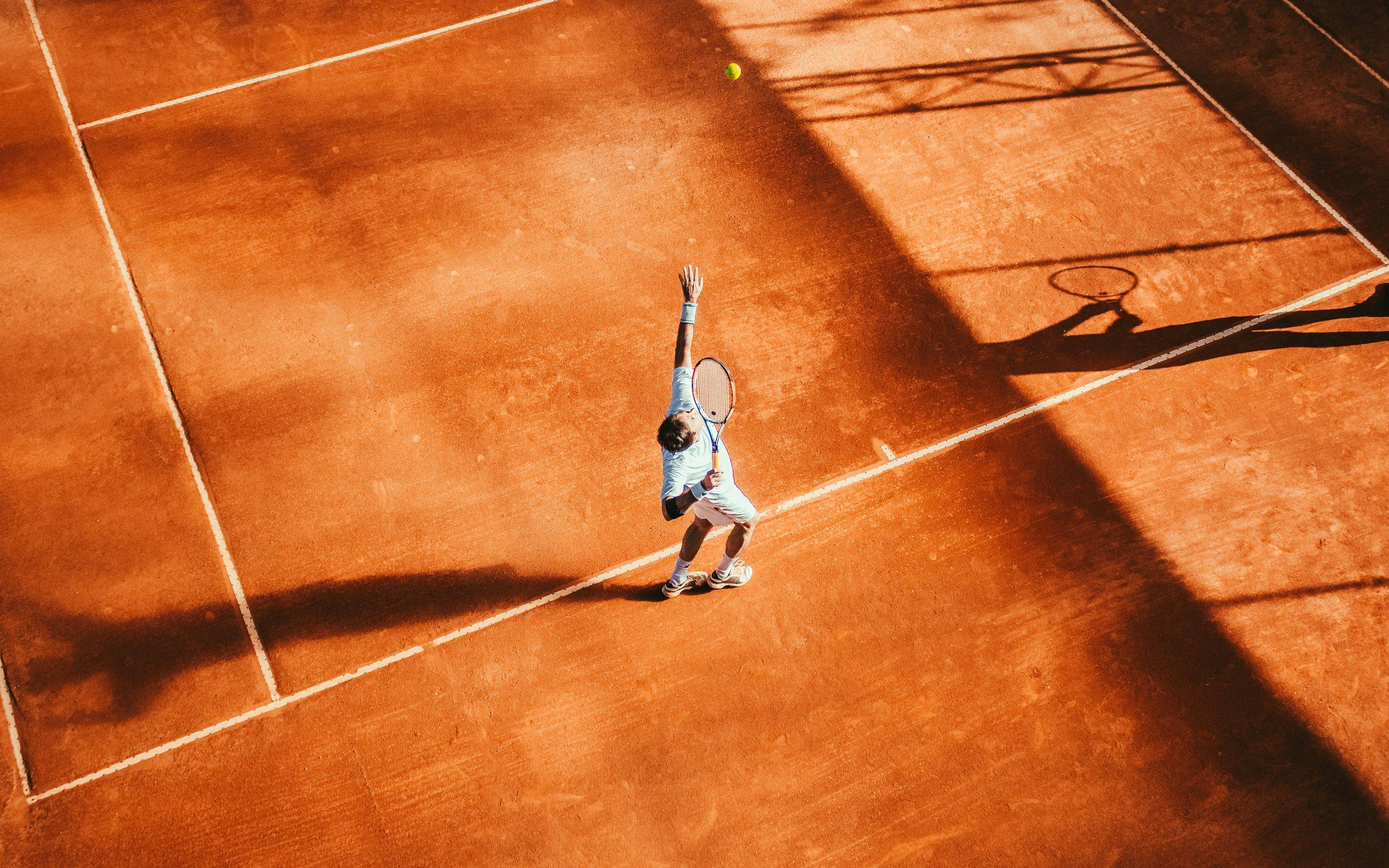 Tenista sacando em quadra de saibro vista de cima